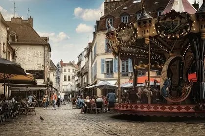 Place pavée animée avec manège, terrasses de café et façades historiques en arrière‑plan.