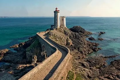 Phare perché au bout d’une jetée rocheuse bordant une mer calme sous un ciel dégagé.