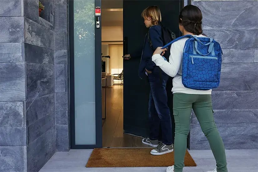 Deux enfants entrant sereinement dans une maison protégée par une alarme porte sécurisant l’accès principal.
