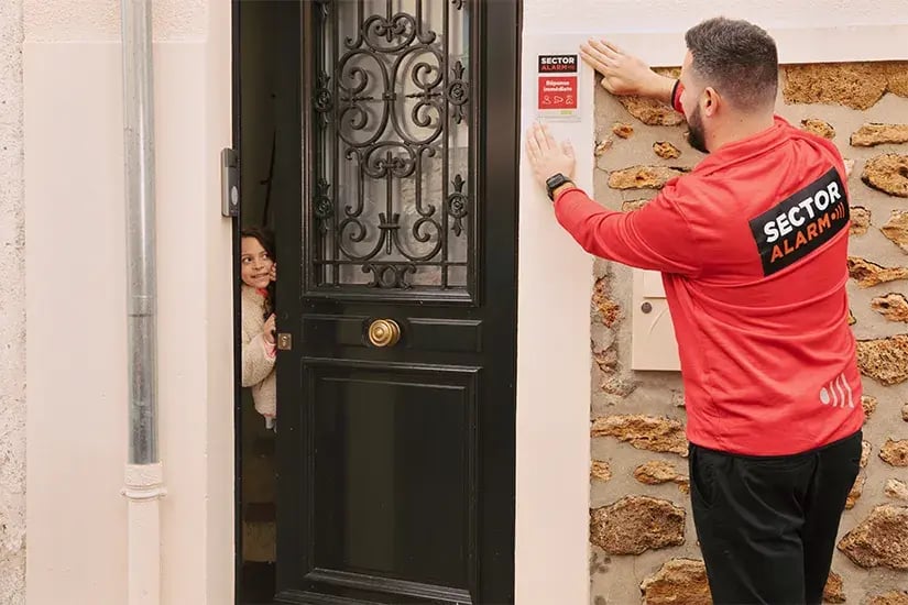Technicien installant une plaque Sector Alarm pour signaler une maison protégée par une alarme maison Technicien installant une plaque Sector Alarm pour signaler une maison protégée par une alarme maison