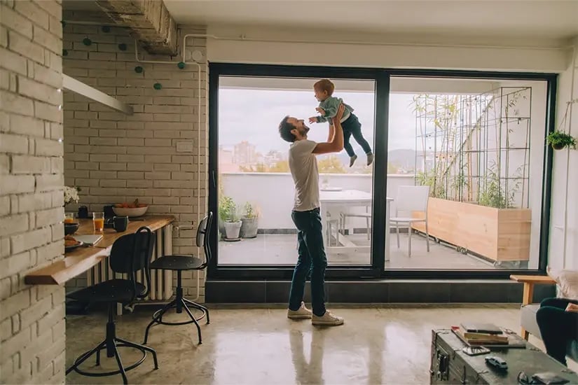 Homme soulevant un enfant serein car protégé des cambriolages en appartement grâce à son alarme. 